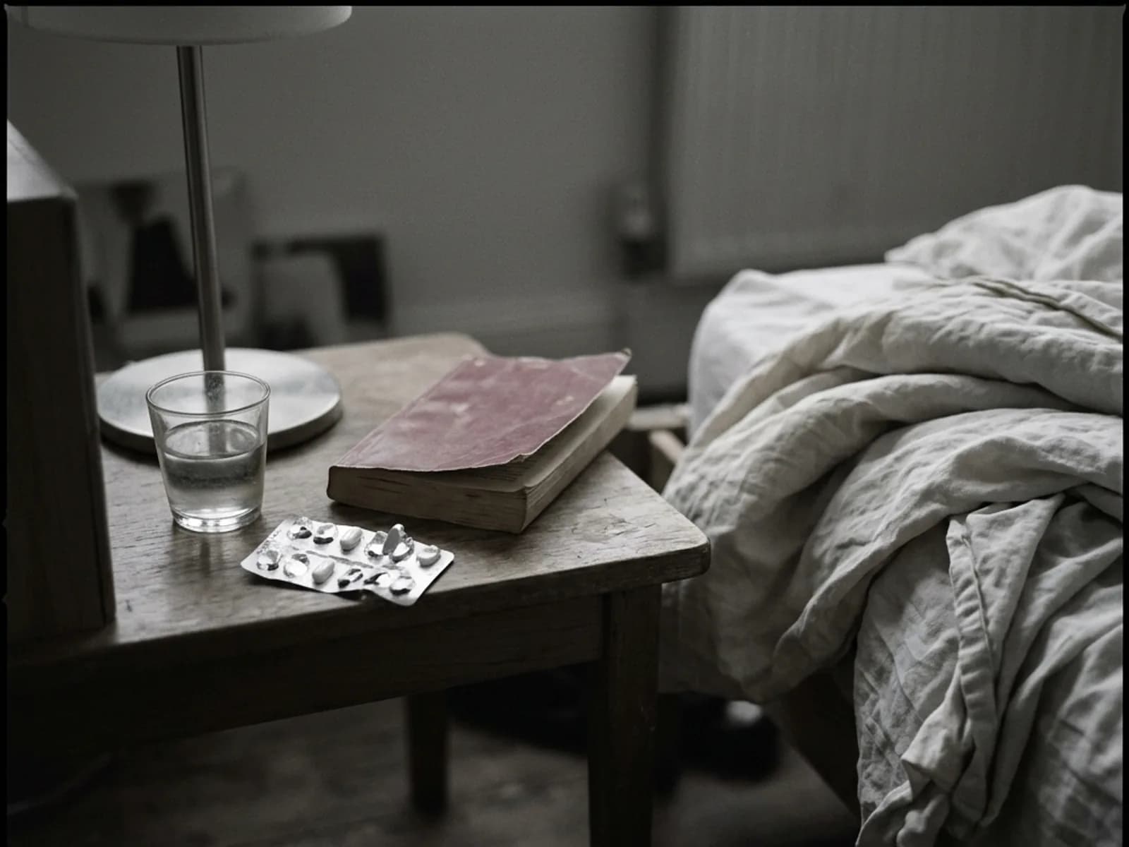 A bedside table in warm evening light with a glass of water, a book, and a lamp.